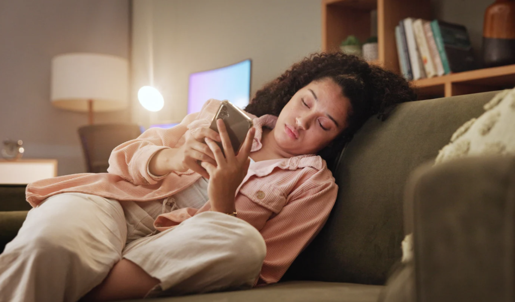 woman sitting on couch looking tired and bored while on her cell phone
